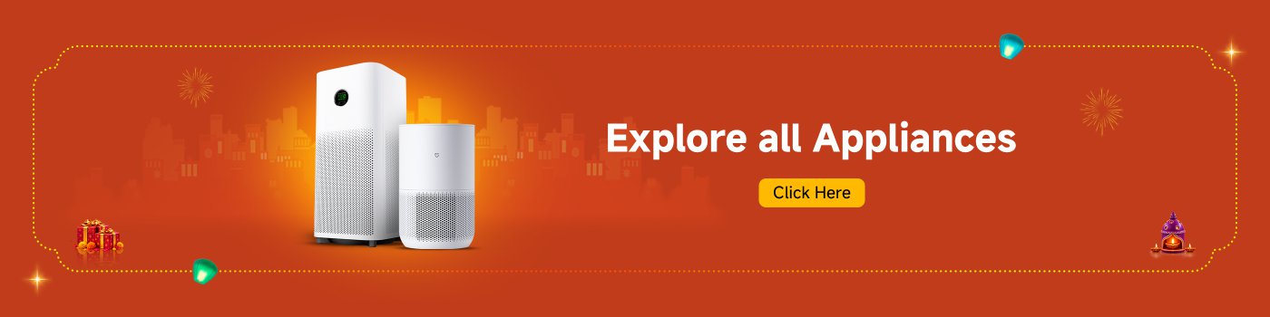Two white home appliances are placed side by side against an orange background, which features festive decorations and gifts. The text reads "Explore All Appliances" and "Click Here."